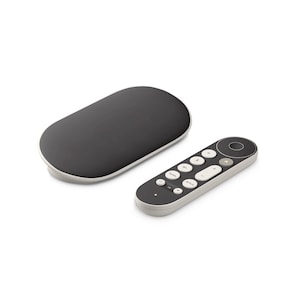 Peut inclure: Un appareil de diffusion multimédia et une télécommande gris foncé. L'appareil de diffusion est de forme ovale avec une bordure gris clair. La télécommande est gris foncé avec des boutons blancs et une commande circulaire en haut.