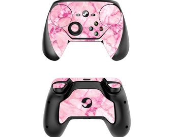 Puede incluir: Un mando Steam de color rosa y negro con un patrón de mármol. El mando tiene un botón circular en el centro y dos joysticks a los lados.