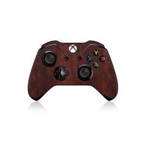 Könnte beinhalten: Brauner Xbox-Controller mit Holzmaserung. Der Controller hat schwarze Knöpfe und ein Steuerkreuz mit farbigen Knöpfen in Gelb, Blau, Grün und Rot. Das Xbox-Logo ist oben sichtbar.