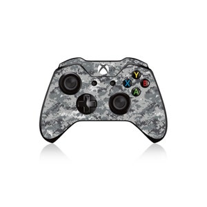 Może przedstawiać: Szary i czarny kontroler Xbox w kamuflażu z czarnymi przyciskami i białym logo Xbox.