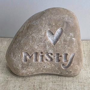 May include: A light brown stone with the word "Misty" carved into it, along with a heart shape.