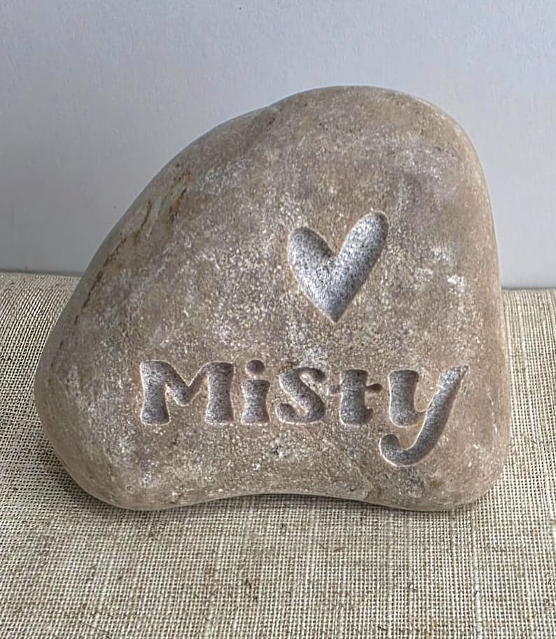 May include: A light brown stone with the word "Misty" carved into it, along with a heart shape.