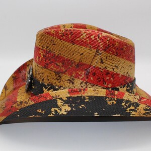 May include: A straw cowboy hat with a distressed red and yellow striped pattern. The hat features a black band and a silver-colored decorative element. The brim has a distressed black pattern.