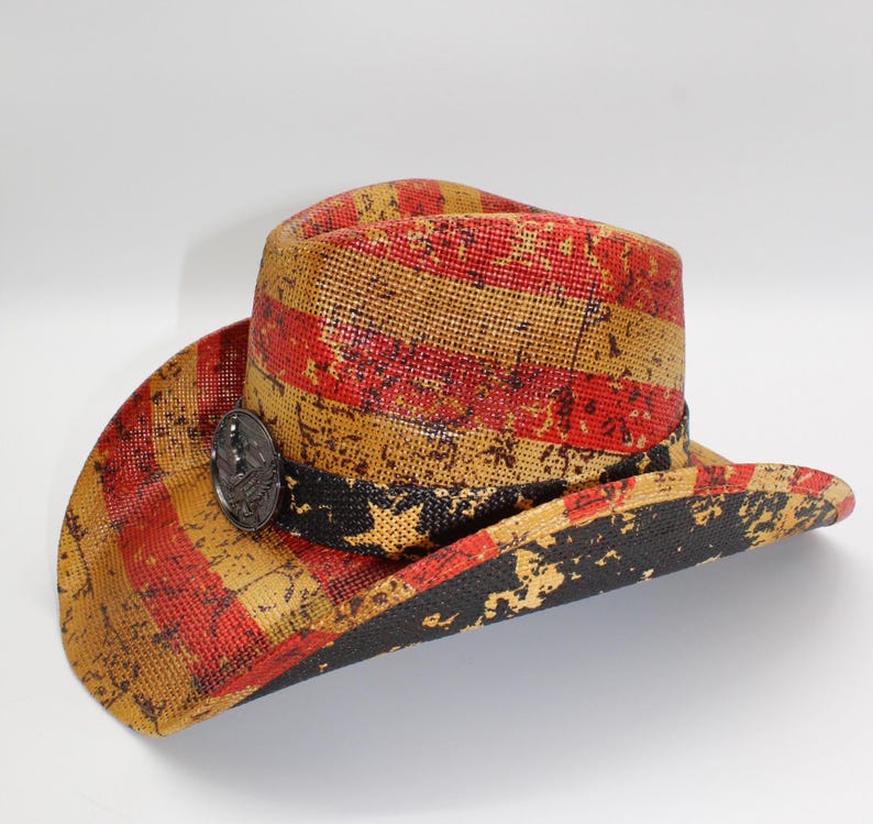 May include: A distressed-look cowboy hat with red and tan stripes, a black band, and a decorative metal emblem. The hat has a wide brim and a structured crown, suitable for sun protection and fashion.