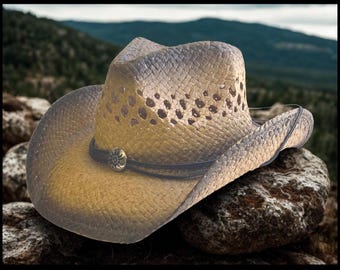May include: A straw cowboy hat featuring a gradient tan and dark brown finish, a pinched crown with ventilation holes, and a dark brown cord hatband accented with a circular metallic concho featuring a sunburst design at the front center.