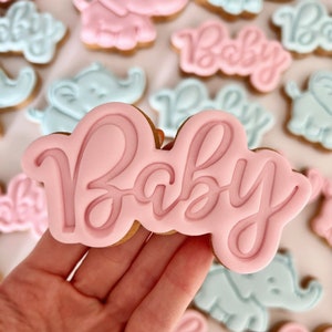 May include: Pink and blue sugar cookies decorated with elephant and baby designs. The cookies are decorated with royal icing and the word "Baby" is written on one of the cookies.