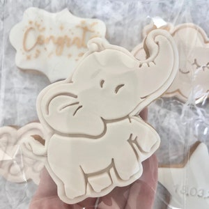 May include: A set of decorated cookies featuring a white elephant, a star with the date "14.03" on it, and a cookie with the word "Congrat" in gold lettering.