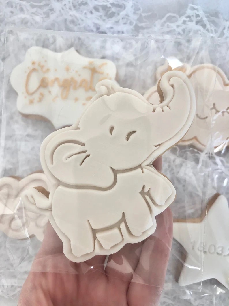 May include: A set of decorated cookies featuring a white elephant, a star with the date "14.03" on it, and a cookie with the word "Congrat" in gold lettering.