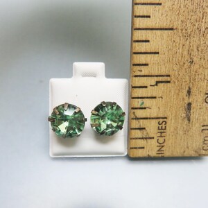 May include: A pair of green glass earrings with a silver setting. The earrings are displayed on a white card with a ruler for size reference.