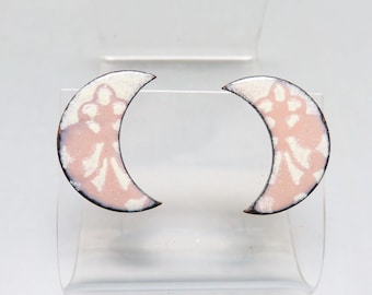 May include: A pair of pink and white enamel crescent moon earrings. The earrings are made of copper and have a delicate floral pattern.