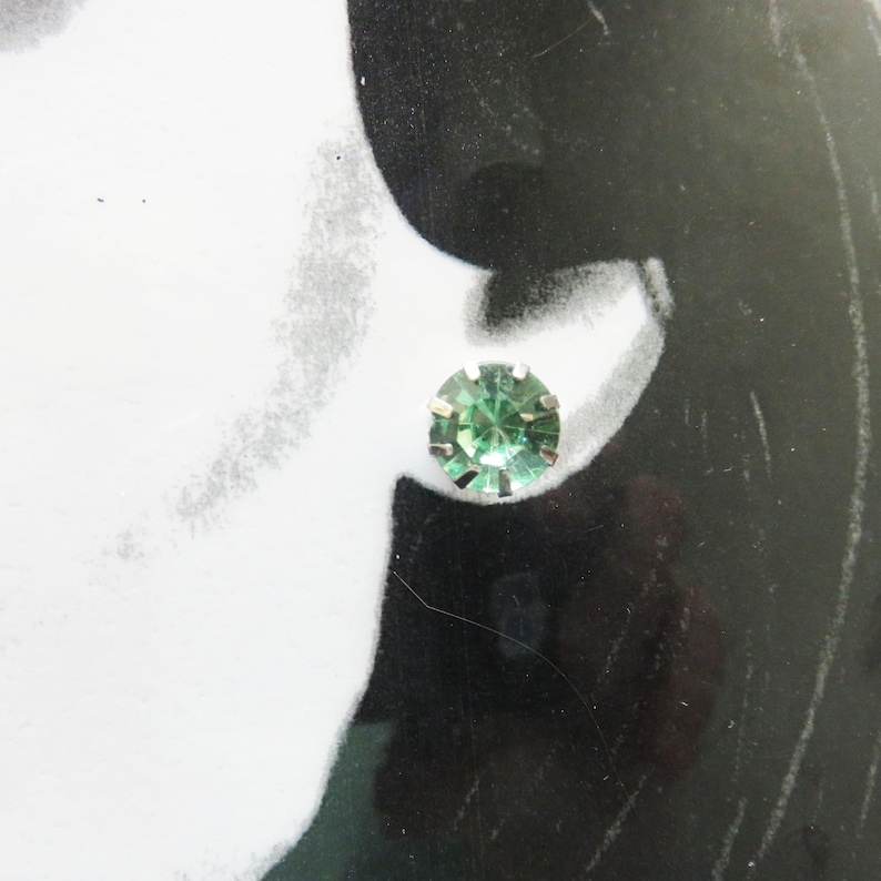 May include: A pair of silver stud earrings with a single green gemstone in each earring.