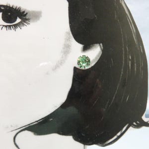 May include: A pair of small, round, green stud earrings. The earrings are set in a silver tone metal.