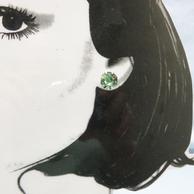 May include: A pair of small, round, green stud earrings. The earrings are set in a silver tone metal.