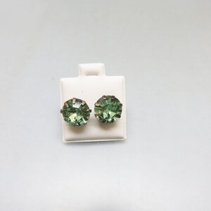 May include: A pair of green gemstone earrings with gold settings. The earrings are displayed on a white card.