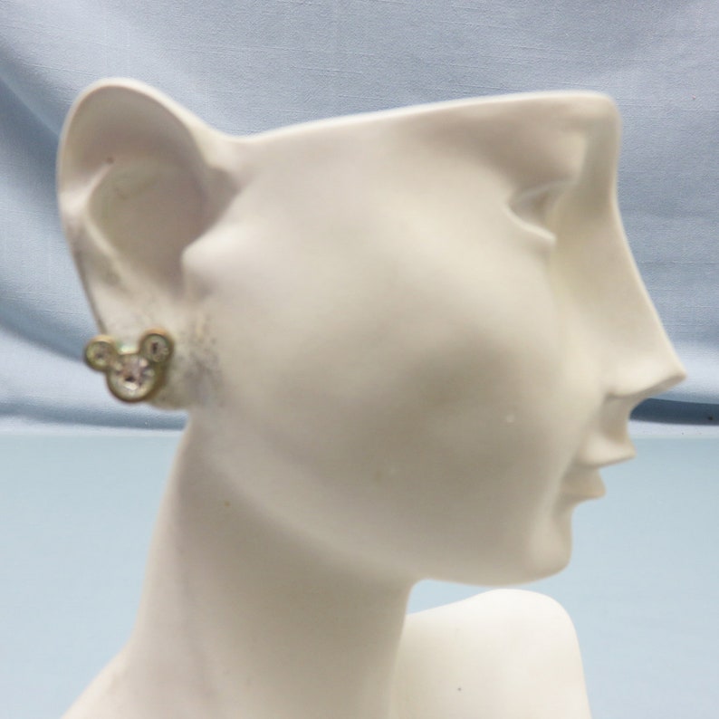 Pode incluir: Brincos de press&atilde;o em tom dourado com uma silhueta de Mickey Mouse adornada com strass transparentes.