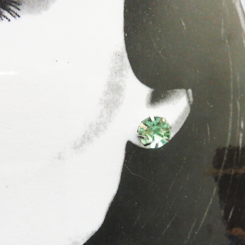 May include: A pair of silver stud earrings with a single, round, light green gemstone in each earring.