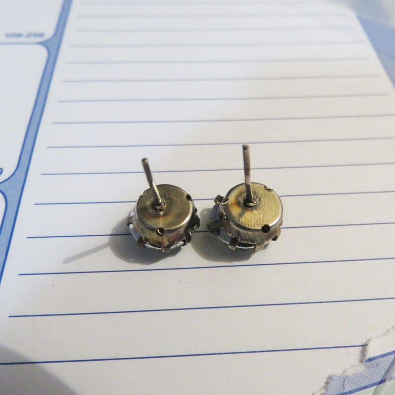 May include: A pair of silver stud earrings with blue gemstones. The earrings are shown from the back, revealing the metal post and butterfly backing.
