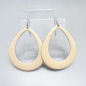 May include: A pair of cream-colored teardrop earrings with silver-tone hooks. The earrings have a smooth, glossy finish and a simple, elegant design. These lightweight earrings are a stylish accessory.