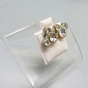 Pode incluir: Um par de brincos de press&atilde;o prateados com cristais de imita&ccedil;&atilde;o transparentes em forma de cabe&ccedil;as do Mickey Mouse.