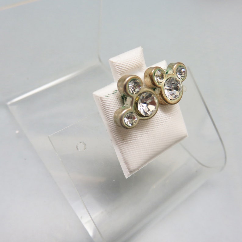 Pode incluir: Um par de brincos de press&atilde;o prateados com cristais de imita&ccedil;&atilde;o transparentes em forma de cabe&ccedil;as do Mickey Mouse.