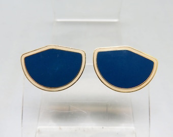 May include: A pair of cufflinks with a gold-colored border and a navy blue center. The cufflinks have a shield-like shape and are displayed on a clear, plastic stand.