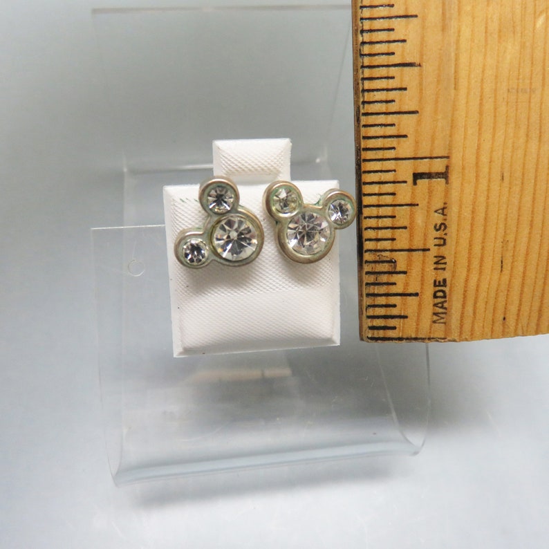 Pode incluir: Um par de brincos de press&atilde;o Mickey Mouse prateados com strass transparentes.