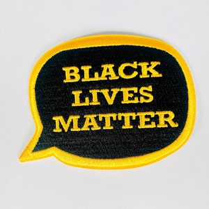 May include: Black Lives Matter embroidered patch in a speech bubble shape with a yellow outline and black background.