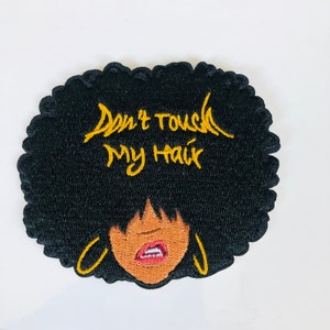 May include: Iron-on patch featuring an embroidered design of a black woman with an afro hairstyle and gold hoop earrings. The text "Don't Touch My Hair" is embroidered in yellow on the patch.
