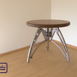 May include: A round wooden table with a silver metal base. The base has a unique design with four legs that are connected by a series of hinges.
