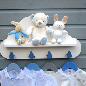 May include: White cloud-shaped shelf with blue raindrop hooks and a white teddy bear, a white bunny, and a Peter Rabbit plush toy on the shelf.  Four blue and gray hangers are hanging from the hooks.