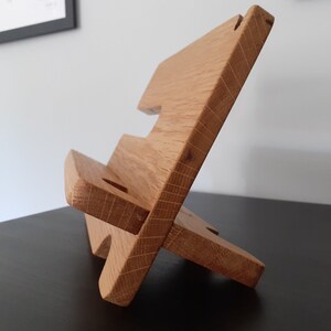 May include: A wooden phone stand with two tiers. The stand is made of light brown wood and has a natural finish.