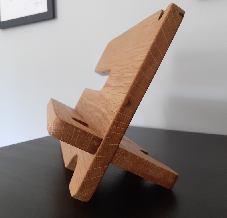 May include: A wooden phone stand with two tiers. The stand is made of light brown wood and has a natural finish.