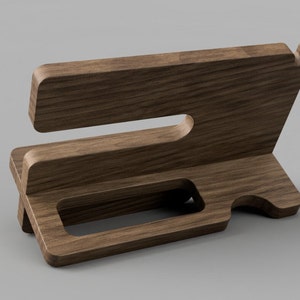 May include: A wooden phone stand with a slot for a phone and a cutout for charging cables. The stand is made of dark brown wood and has a natural wood grain.