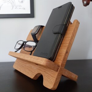 May include: A wooden phone stand with a black phone case, glasses, and a watch on it.