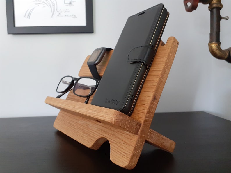May include: A wooden phone stand with a black phone case, glasses, and a watch on it.