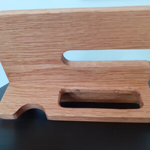 May include: A wooden stand with two slots for holding items, such as phones or tablets. The stand is made of light brown wood and has a natural finish.