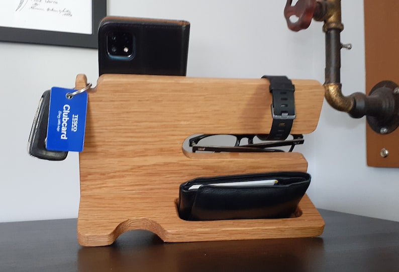 May include: Wooden organizer with slots for a phone, watch, glasses, and wallet. The organizer is made of light brown wood and has a blue Tesco Clubcard attached to it.