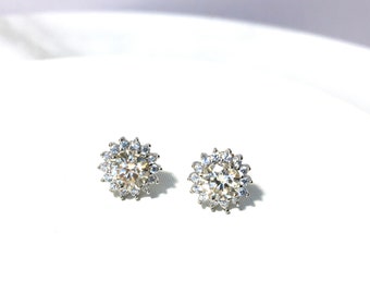 May include: A pair of silver stud earrings with a round, clear stone surrounded by smaller clear stones.