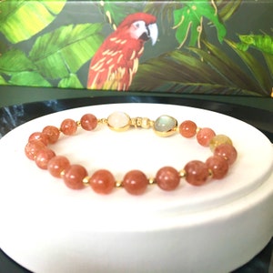 Puede incluir: Un brazalete hecho de peque&ntilde;as cuentas redondas de color marr&oacute;n anaranjado con dos cuentas redondas m&aacute;s grandes de color claro y un cierre dorado.