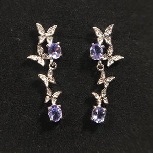 May include: A pair of silver dangle earrings with butterfly designs and purple gemstones.