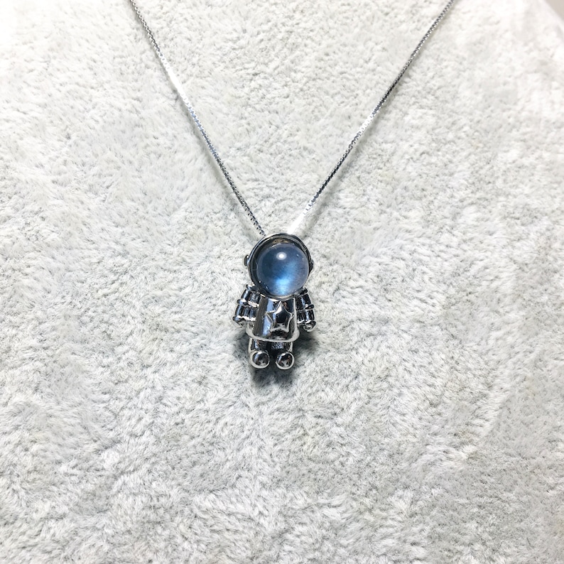 Puede incluir: Un collar de plata con un peque&ntilde;o colgante de astronauta. La cabeza del astronauta es una piedra preciosa azul.