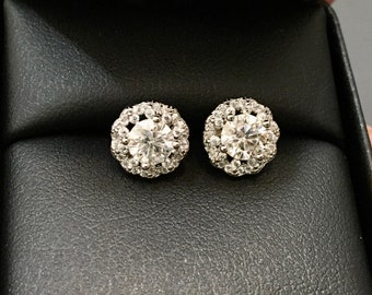 May include: A pair of silver stud earrings with a round, clear diamond center surrounded by a halo of smaller diamonds.
