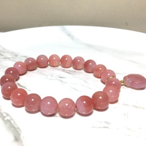 May include: A pink gemstone bracelet with a pink gemstone charm. The bracelet is made of round beads and has a gold clasp.