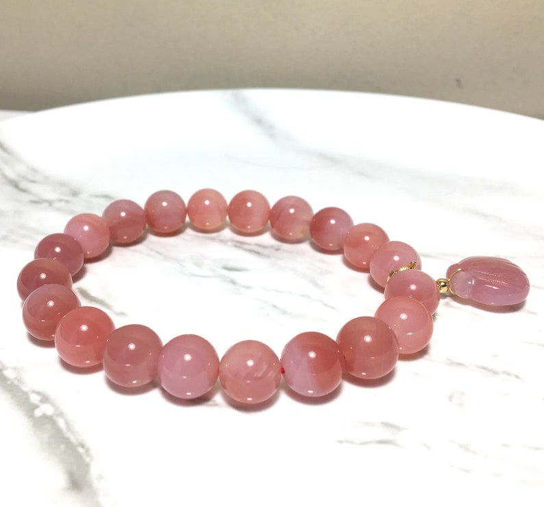 May include: A pink gemstone bracelet with a pink gemstone charm. The bracelet is made of round beads and has a gold clasp.