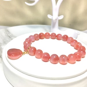 May include: A pink agate gemstone bracelet with a matching pendant. The bracelet is made of round beads and has a gold clasp.