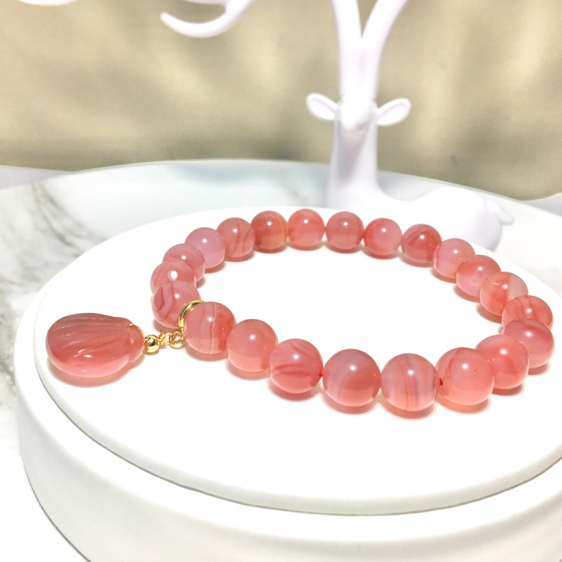 May include: A pink agate gemstone bracelet with a matching pendant. The bracelet is made of round beads and has a gold clasp.