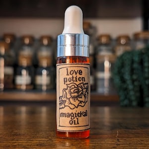 Może przedstawiać: Mała szklana butelka ze srebrną zakrętką i brązową etykietą z napisem "love potion magickal oil". Etykieta zawiera czarno-biały rysunek róży.