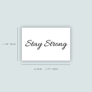 Puede incluir: Tarjeta blanca con el texto "Stay Strong" escrito en cursiva negra. La tarjeta mide 4,5 cm por 3 cm.