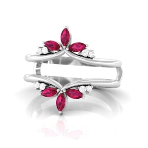 Puede incluir: Un protector de anillo de plata con dos bandas simétricas unidas por un puente. Cada lado está adornado con rubíes de color rosa intenso en talla marquesa y pequeños diamantes blancos redondos dispuestos en un patrón floral sobre el metal.