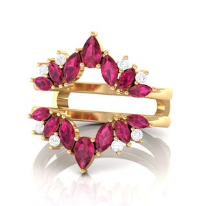 Könnte beinhalten: Ein goldfarbener Ringschutz mit Doppelband-Design. Der Ring ist mit marquise- und tropfenförmigen Rubin-Edelsteinen sowie runden, klaren Edelsteinen besetzt. Die Edelsteine sind in einem floralen Muster angeordnet.